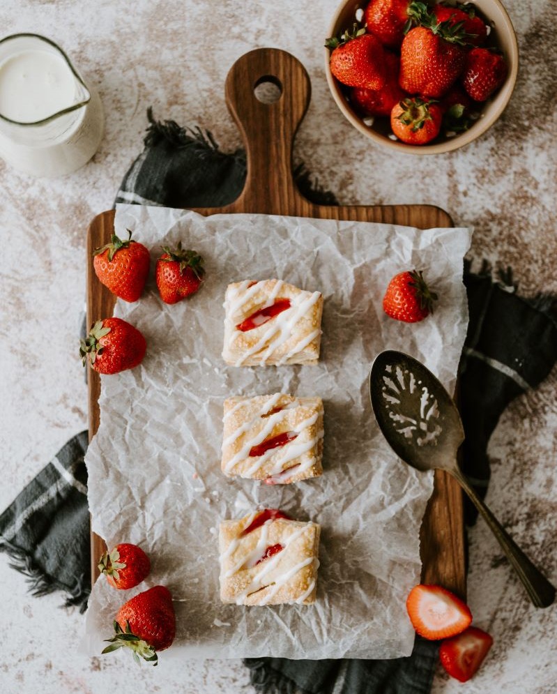 Three Strawberry Cream Pastry Puffins on a wood serving board, surrounded by strawberries.