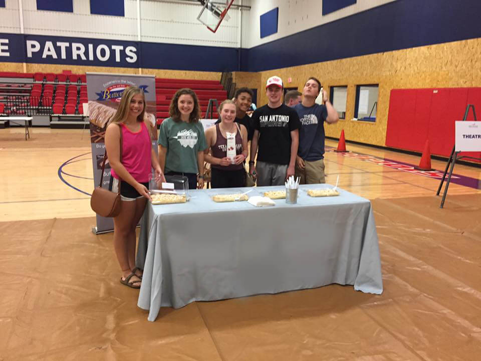 Group of high school kids at a fundraising kick off in their school auditorium. Several baked pastries are on a table for sampling.