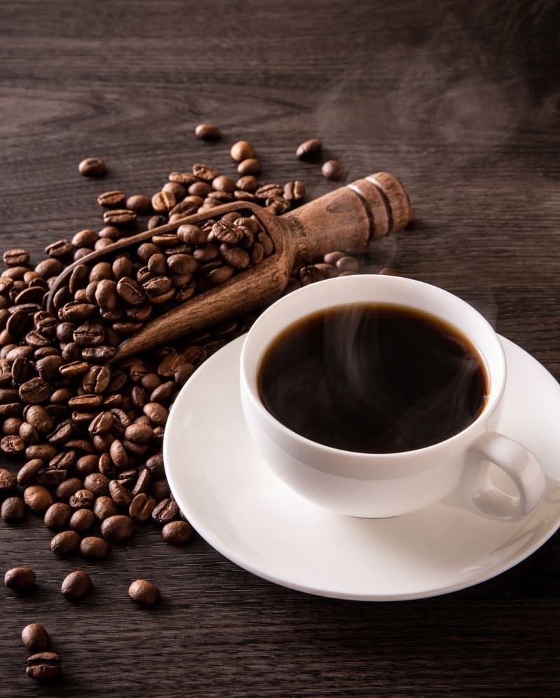 A cup of steaming coffee next to several coffee beans.